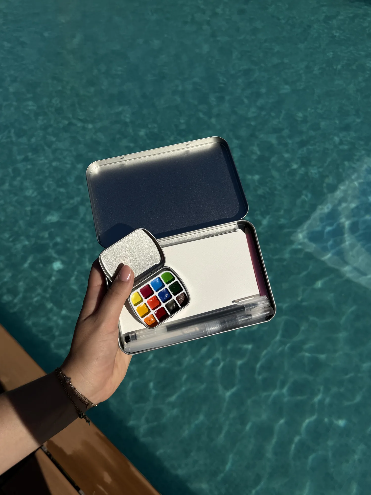 Open Tinybesos watercolor kit held above the water
